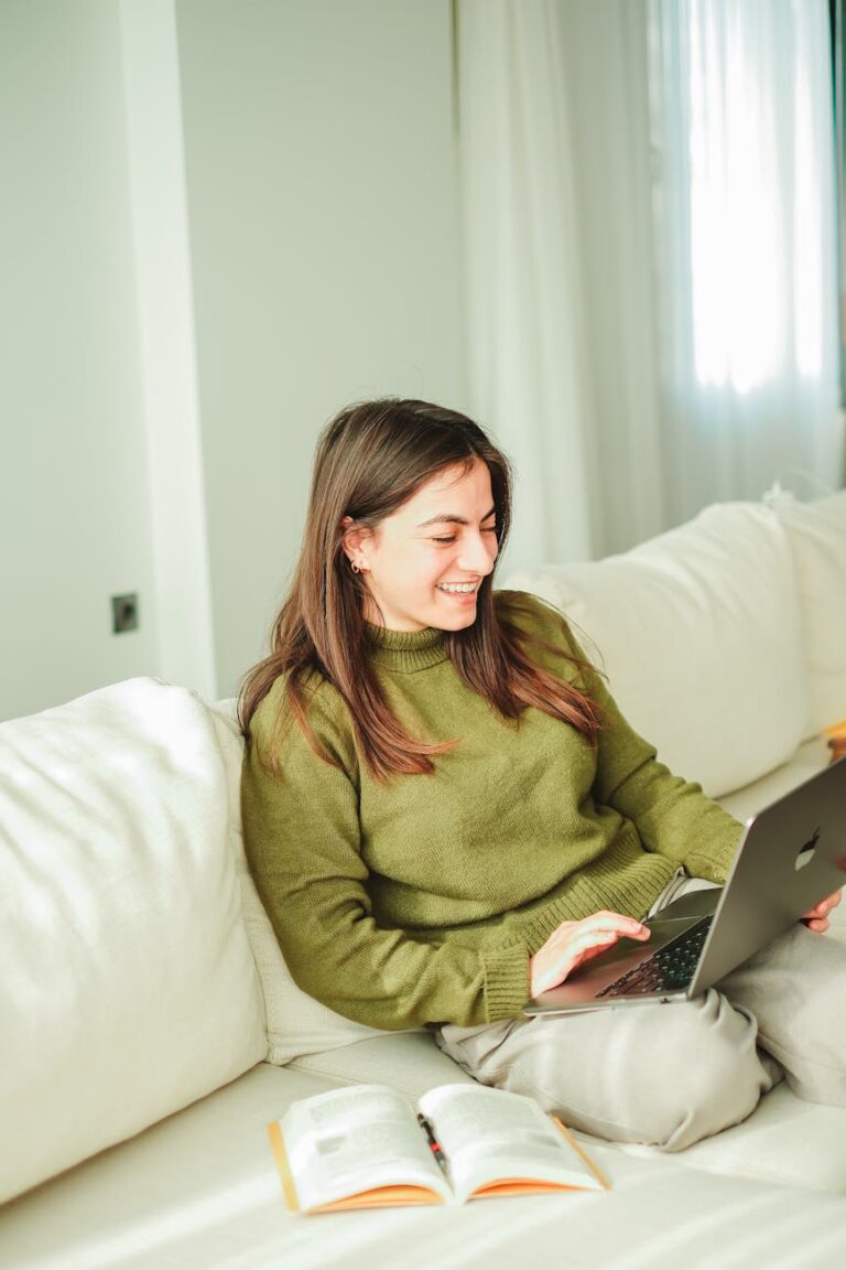 pexels-photo-19546262-19546262 | Freedom For You 2 A young woman enjoys working on her laptop while relaxing on a sofa indoors, surrounded by books.